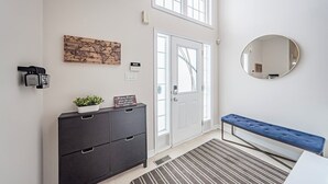 Un hall d’entrée moderne avec un meuble en bois foncé, un panneau d’accueil, un miroir fixé au mur et un banc.