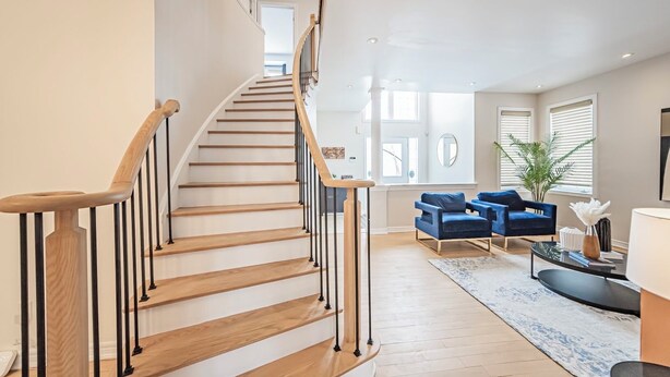 Un vaste espace de vie agrémenté d’un escalier en bois, de canapés bleus et d’une table basse.