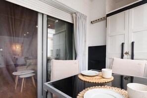 Une chambre moderne avec une cloison en verre, une petite table ronde sur laquelle se trouvent une assiette et une tasse, et une chaise avec un coussin.