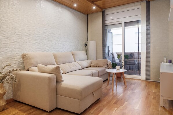 Un salon moderne avec un canapé d’angle beige, une petite table ronde et un mur blanc orné d’un motif texturé.