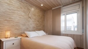 A bedroom with a bed, a nightstand, a lamp, and a window. - Quiet apartment Tossa de Mar (Tossa de Mar)