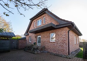Een tweelaags bakstenen huis met een puntig dak, een voordeur en een lage stenen muur ervoor.