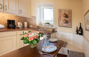 Een keuken met een eettafel voor twee personen, een koffiezetapparaat en een vaas met bloemen.