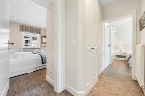 A hotel room with a bed, a nightstand, a dresser, and a window with blinds. - Maison Borelör, Apt. 1 - Spacious 3-room apartment of approximately 80 m² for up to 4 people (Sylt)