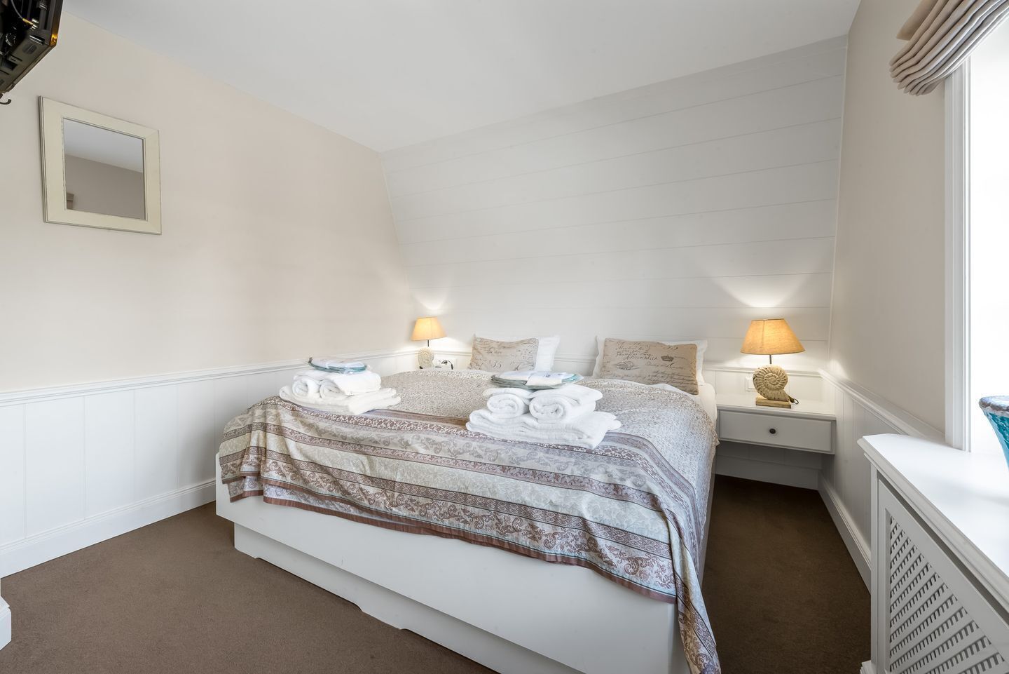 Een hotelkamer met een bed, twee nachtkastjes, een spiegel en een raam met gordijnen.