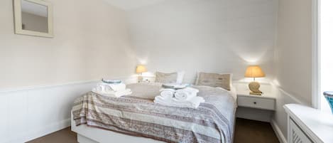 A hotel room with a bed, two bedside tables, a nightstand, a mirror, and a window with curtains.