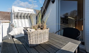Rottingista punottu kori, jossa on kasveja, on asetettu puupöydälle rakennuksen ulkopuolelle. Rakennuksen yläpuolella on kyltti, jossa lukee ”Sonnenraum”.