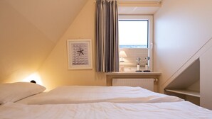 A bedroom with two beds, a window with curtains, a radiator, and a clock on the wall. - Haus Sonnentraum, Whg. 2 - Sun-flooded 2-room apartment on approx. 60 m² for (Sylt)
