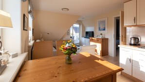 A modern kitchen with white cabinets, a wooden dining table with a vase of flowers, and a view to the outside. - Haus Sonnentraum, Whg. 2 - Sun-flooded 2-room apartment on approx. 60 m² for (Sylt)