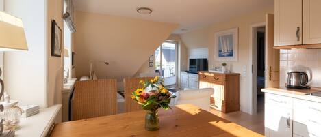 A modern kitchen with white cabinets, a wooden dining table with a vase of flowers, and a view to the outside.