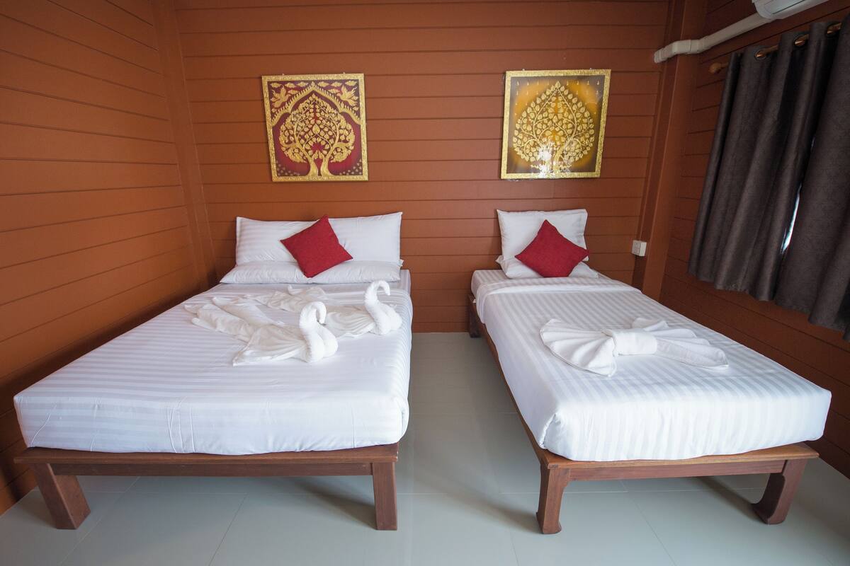 Duas camas de solteiro com roupa de cama branca e almofadas vermelhas, cabeceiras de madeira e arte decorativa na parede.
