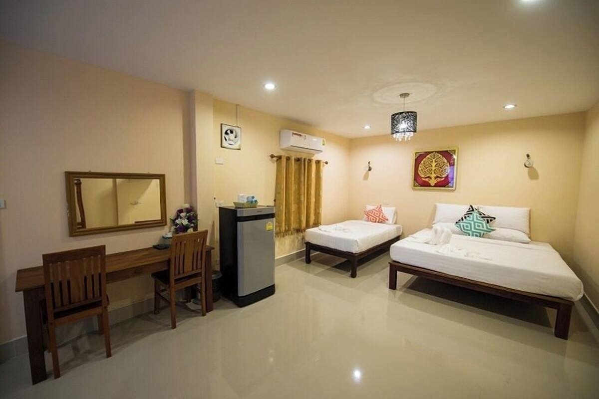 Quarto de hotel com escrivaninha, duas camas de solteiro, um pequeno frigorífico e um aparelho de ar condicionado.