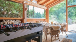 A wooden-floored room with a foosball table, wicker chairs, and a large window overlooking greenery. - Dendron by Interhome (Ovronnaz)