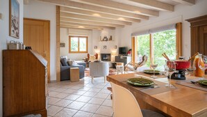 A spacious living area with a wooden ceiling, a dining table set with plates and glasses, and a television in the background. - Dendron by Interhome (Ovronnaz)