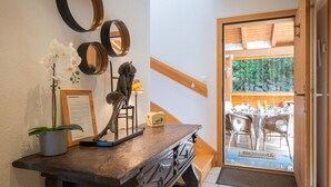 A wooden desk with a potted orchid, a framed picture, and a sculpture. A wooden door leads to an outdoor area with a table and chairs. - Dendron by Interhome (Ovronnaz)