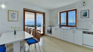 Une cuisine moderne avec des meubles blancs, une cuisinière, un four et un lave-vaisselle. On y trouve une table à manger avec des chaises bleues et un vase rempli de fleurs.