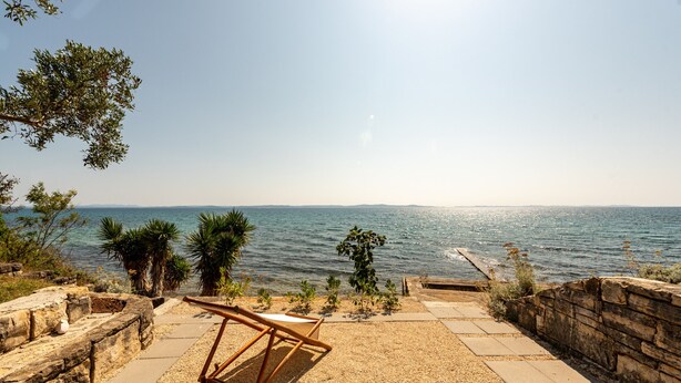 Une terrasse en bord de mer offrant une vue sur l’océan, une chaise en bois et un mur en pierre.