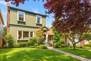 A two-story house with a front porch, a well-maintained lawn, and a tree with red leaves. - Anne Haven Spacious Retreat DT Seattle (Seattle)