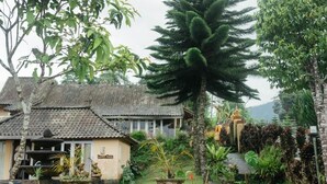 A traditional house with a tiled roof, surrounded by lush greenery and a large tree.
