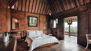 A wooden cabin with a large bed, a wooden table, and a balcony.