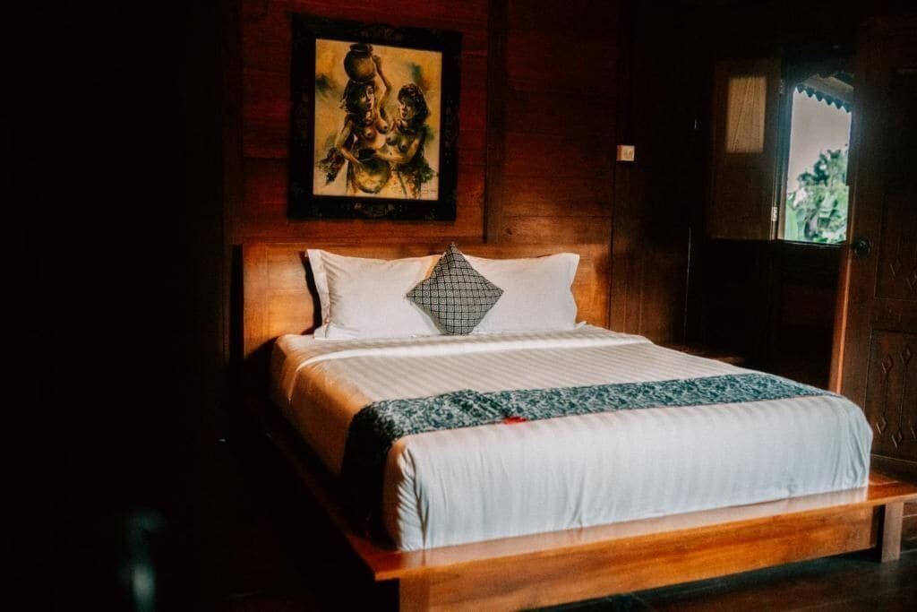 A wooden bed with a white and patterned bedspread, a decorative pillow, and a framed artwork above the bed.