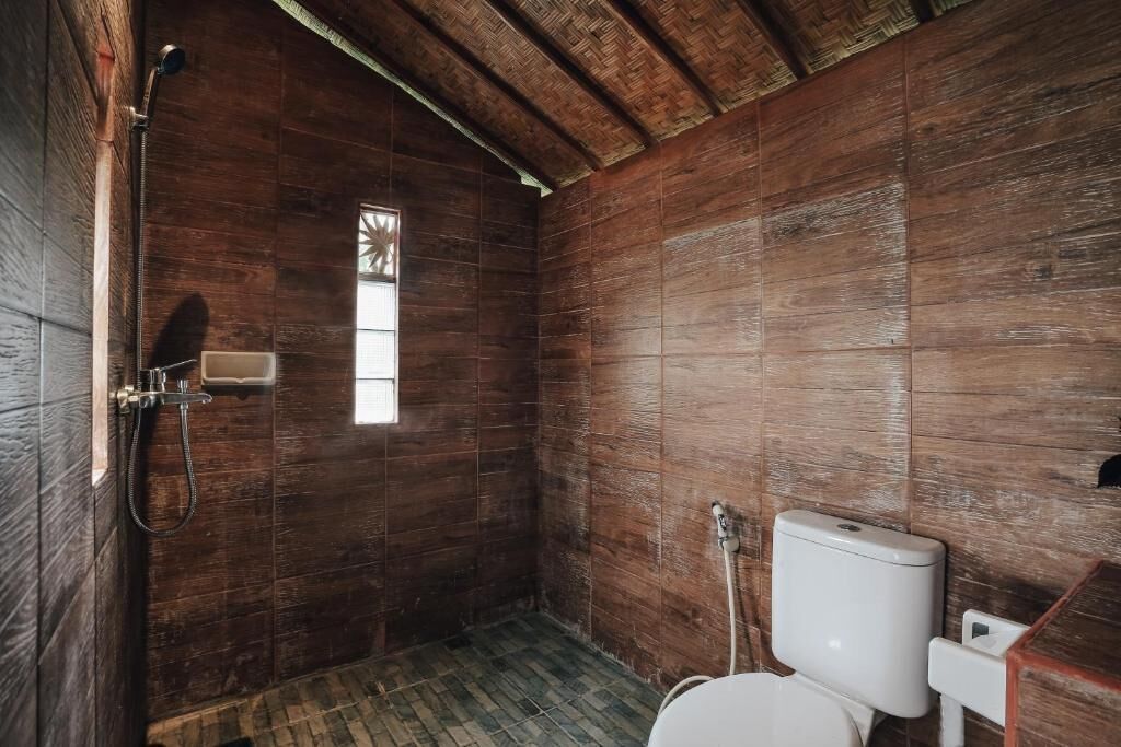 A wooden-paneled bathroom with a shower, toilet, and a small window.