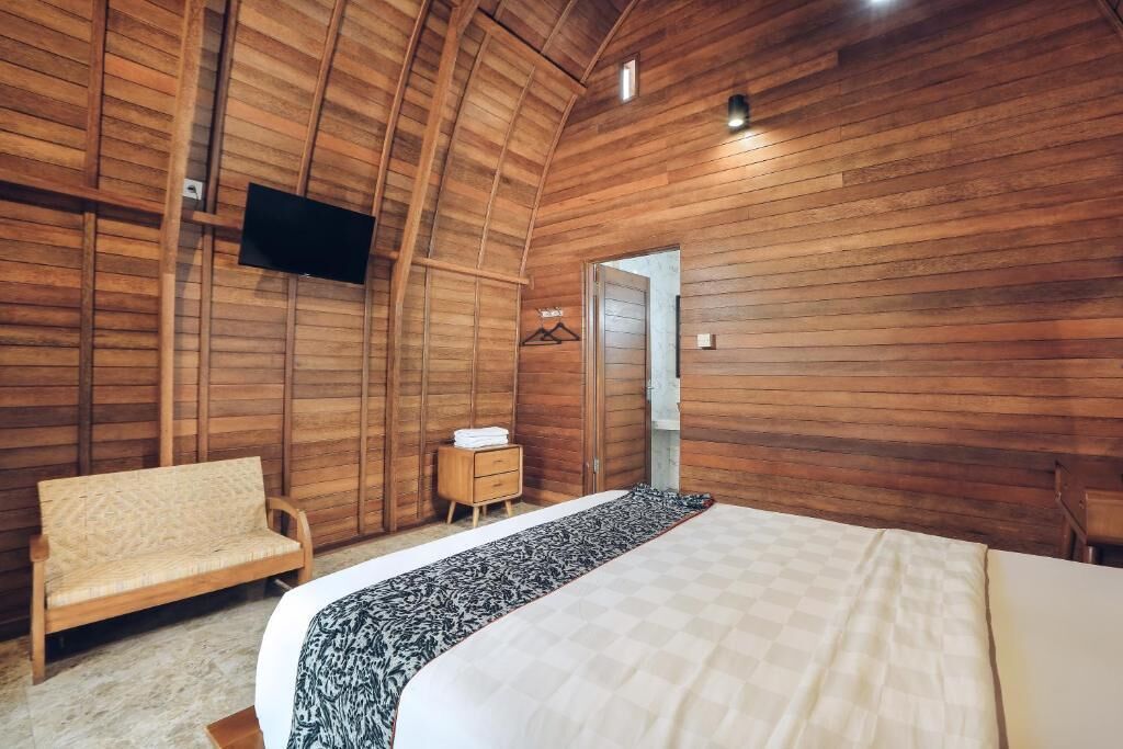Un dormitorio con paredes de madera, una cama, un sofá, un televisor y una mesita.