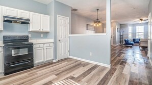 A modern kitchen with white cabinets, a black stove, and a wooden floor.