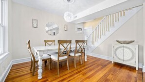 Une salle à manger avec une table blanche et des chaises en bois, un escalier et un luminaire décoratif au plafond.