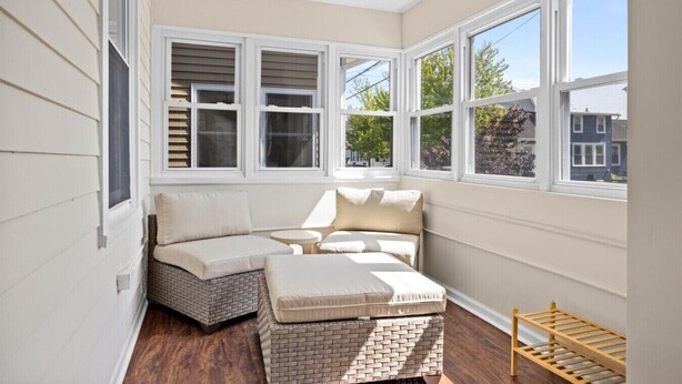 Une véranda dotée d’une banquette intégrée et d’un pouf, de grandes fenêtres et d’une étagère en bois.