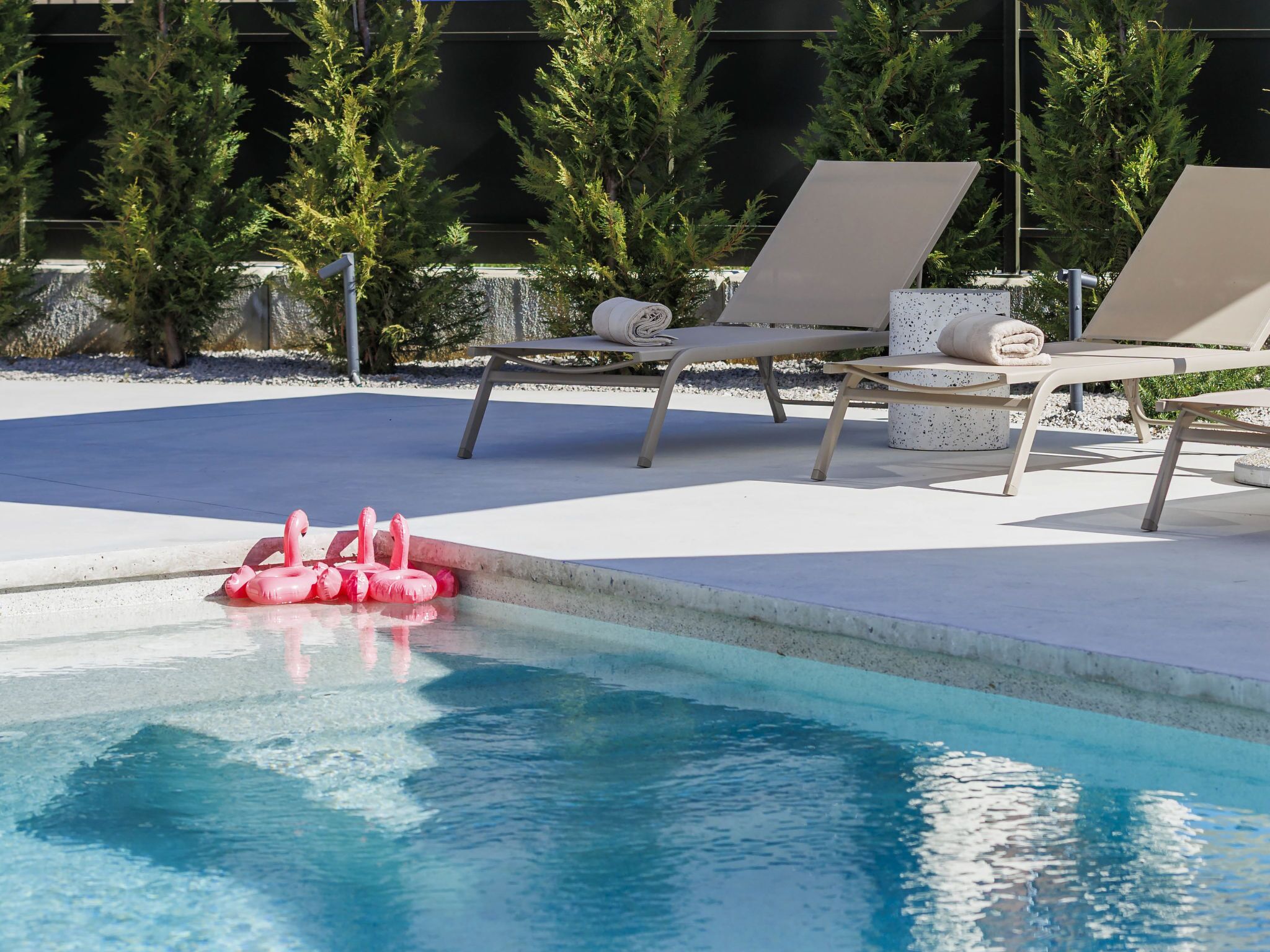 En pool med solstolar och rosa uppblåsbara flamingos.