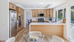 Une cuisine moderne avec des meubles en bois, des appareils en acier inoxydable et une table à manger en verre.