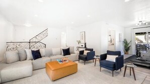 Un salon moderne avec un canapé, des fauteuils, une table basse et un escalier.