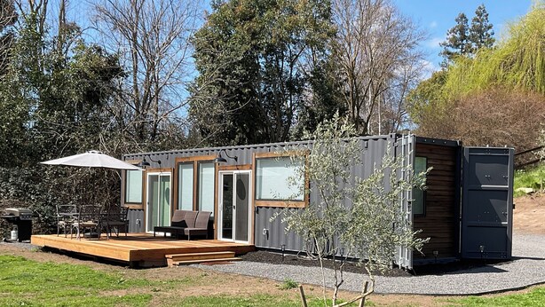 A modern container home with a deck, outdoor seating, and a small garden area.