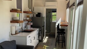 A compact kitchen with a refrigerator, stove, and microwave. There is a dining area with a table and chairs. The room has a ceiling fan and a TV mounted on the wall.