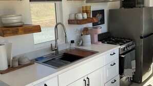 A modern kitchen with white cabinets, a stainless steel refrigerator, a gas stove, and wooden shelves above the counter.
