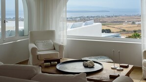 A modern room with a white sofa, a wooden coffee table, and a view of the sea and landscape. - Soho Villa in Paros (Tzanes)