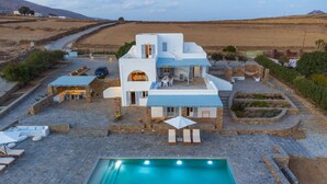 A modern villa with a swimming pool, outdoor seating, and a stone patio. - Soho Villa in Paros (Tzanes)