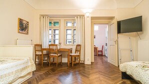 A room with a wooden floor, a bed with a floral bedspread, a table with chairs, a window with curtains, and a television mounted on the wall. - 1 Bed Flat - Sleeps 4 - Pets - Wifi (Praha)