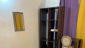 Ein Schlafzimmer mit einem Bett, einem Nachttisch aus Holz, einem kleinen Tisch, einem Stuhl, einem Kleiderschrank und einem Spiegel.