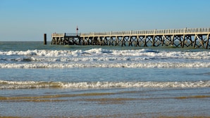 A pier extending into the ocean with a bench and a red flag. - Le Reflet Marin (Saint-Jean-de-Monts)