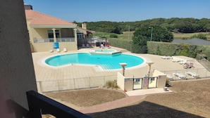 A pool area with a circular pool, lounge chairs, and a view of a golf course. - Le Reflet Marin (Saint-Jean-de-Monts)