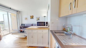 A modern kitchen with white cabinets, a microwave, and a stainless steel sink. - Le Reflet Marin (Saint-Jean-de-Monts)