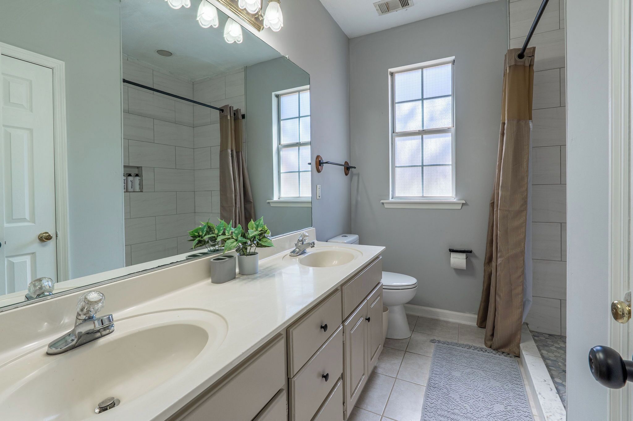 A bathroom with a double sink vanity, a toilet, a shower with a curtain, and a large mirror.