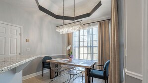 Uma área de refeições com bancada de mármore, um candelabro e uma janela grande com cortinas.