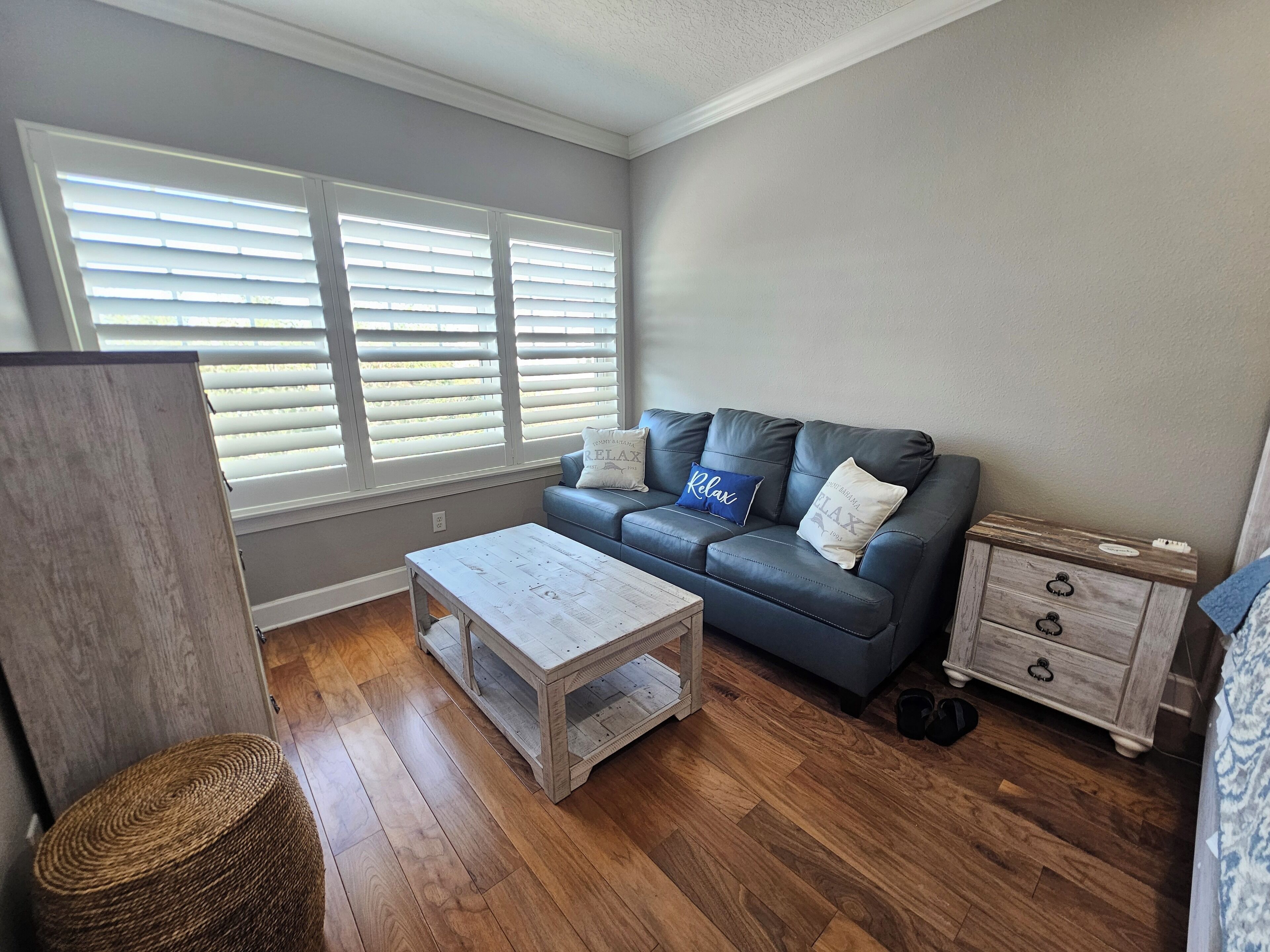 Una sala de estar con un sofá gris, dos almohadas, una mesita de centro, una mesita de noche de madera y una cesta de mimbre.