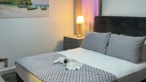 Un lit bien fait, recouvert d’une couvre-lit à motifs, avec une lampe de chevet et un ventilateur de plafond.