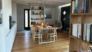 Una cocina moderna con suelo de madera, un comedor con mesa y sillas de madera, una estantería con libros y una puerta negra.
