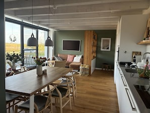 A modern kitchen with a dining area, large windows, and a view of the outdoors.