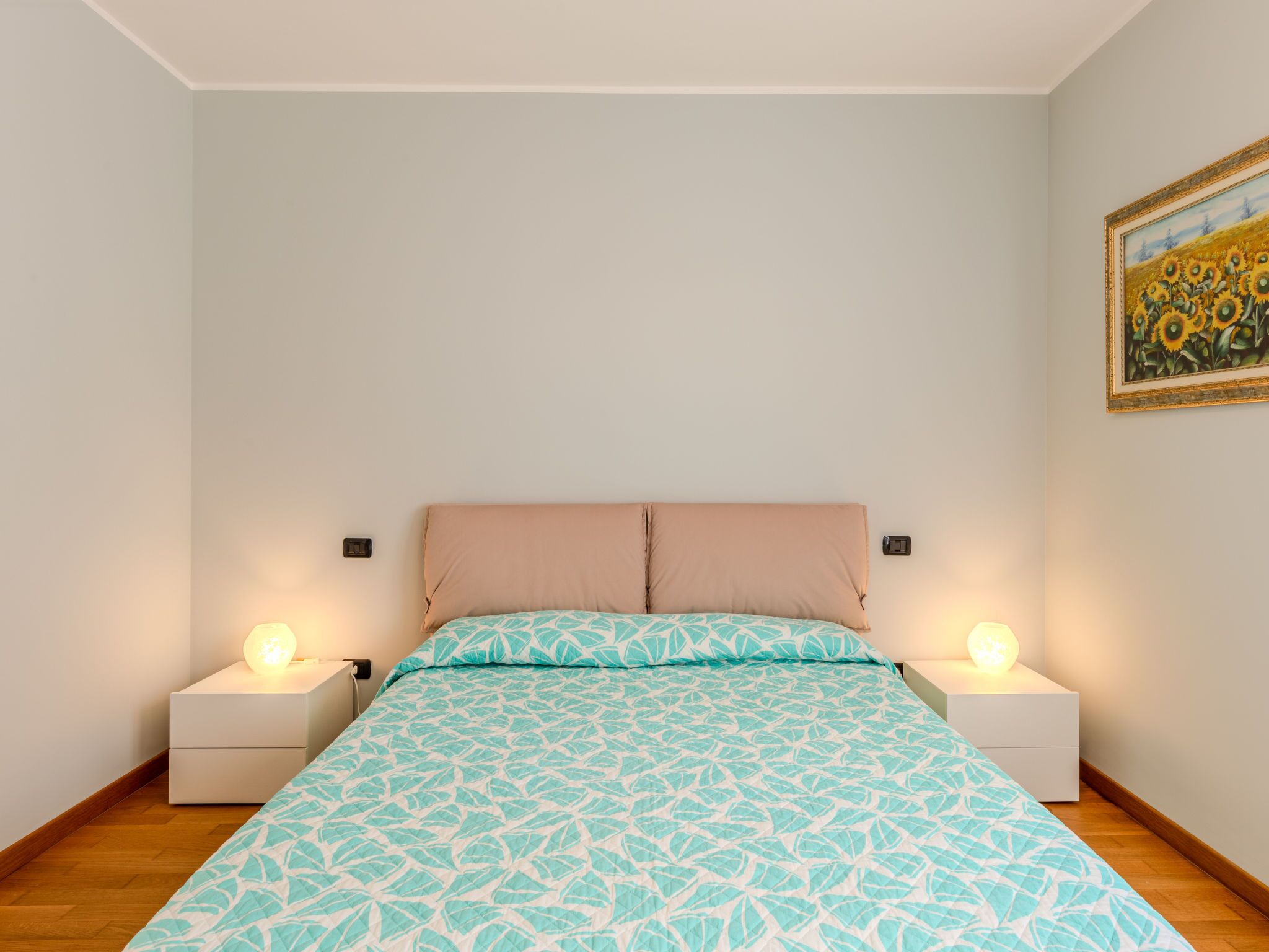 Une chambre à coucher avec un lit, deux tables de chevet avec des lampes, un tableau au mur et un plancher en bois.